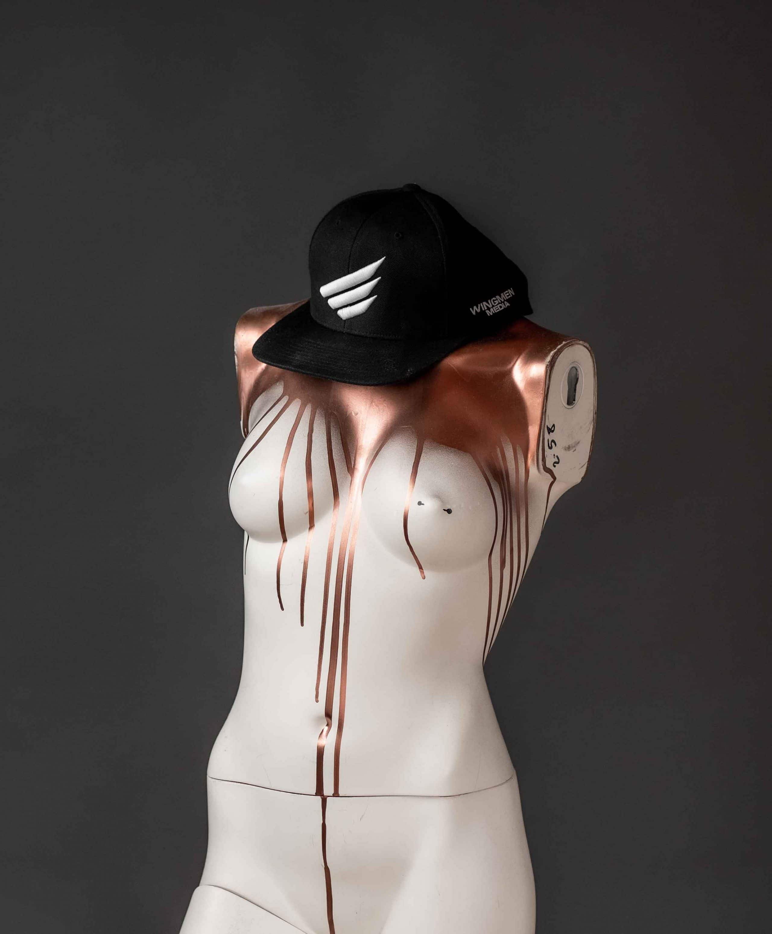Eine Schaufensterpuppe ohne Arme und Kopf, mit Bronze, Metaleffect Farbe überlaufen, trägt ein WINGMEN Media Cap, Logo, Schrift, Unternehmensfotografie, WINGMEN Media