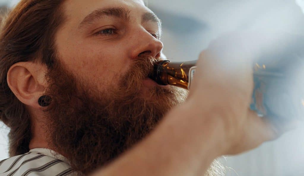 Ein Mann Mit Vollbart trinkt ein Bier, Haare, Barbershop, steinzeit für haare, Recruitingfilm, WINGMEN Media