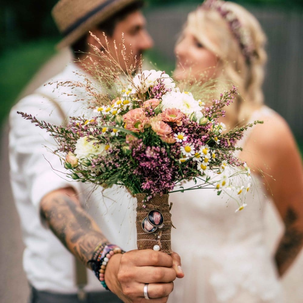 Ein Brautpaar, Bräutigam hält den Brautstrauß nach vorne, Blumen, Ehering, Hochzeit, Event Fotografie, WINGMEN Media
