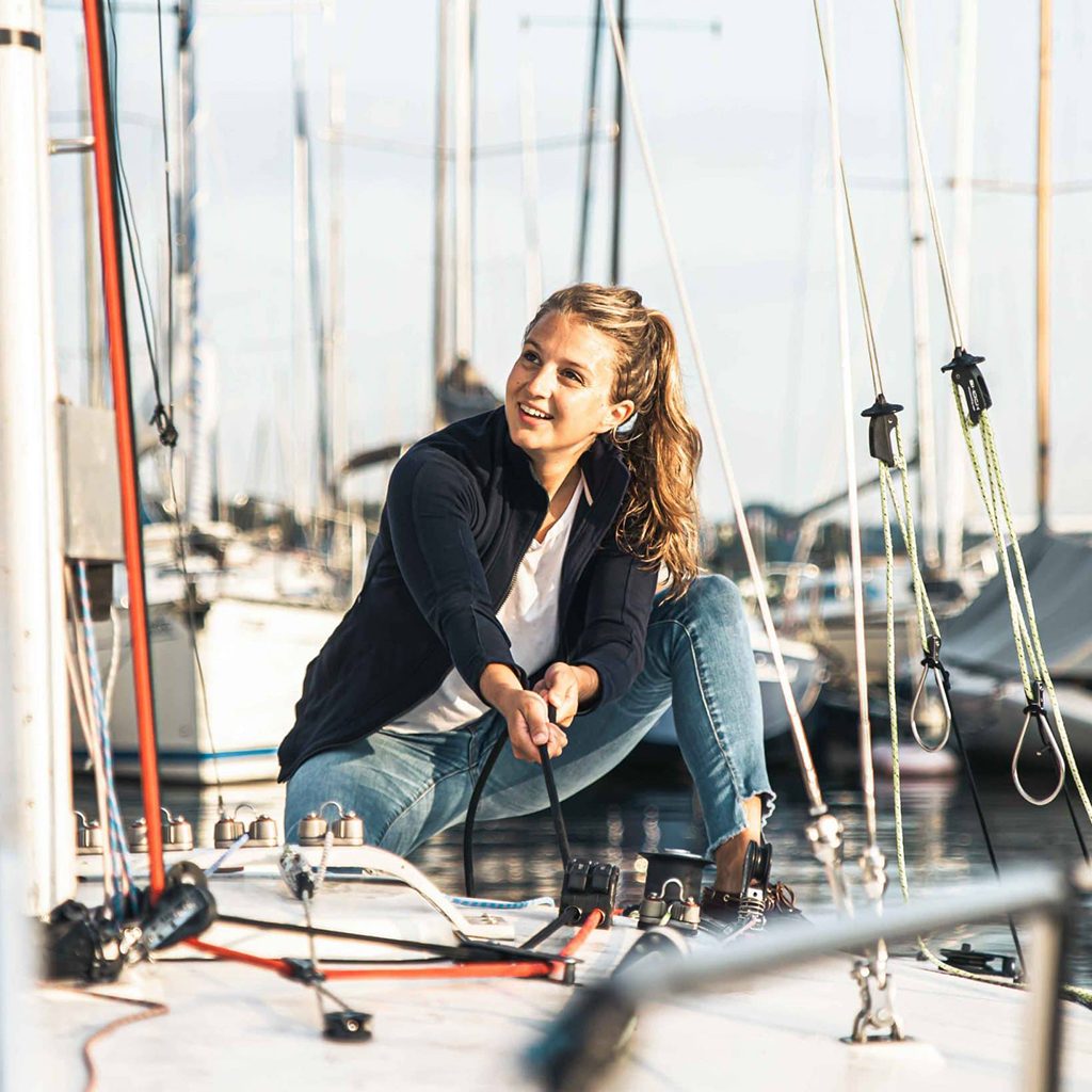 TOURISMUSFILM 51 Eine junge Frau zieht das Segel hoch auf Segelboot im Sportboothafen Stippelwirft in Prien am Chiemsee, Prien Tourismus GmbH, Tourismuskampagne, Lifestylefotografie, WINGMEN Media