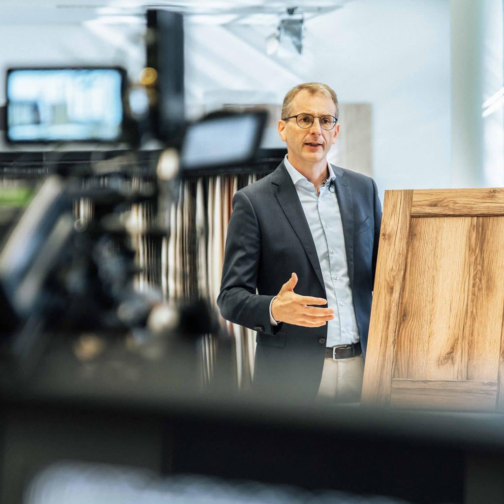 PRODUKTFILM 50 Behind the scenes Aufnahme einer Person bei der Präsentation der Funktionen und Designs des Holzdekors, helles Dekor mit Holzoptik, Schattdecor, Behind The Scenes Fotografie, WINGMEN Media