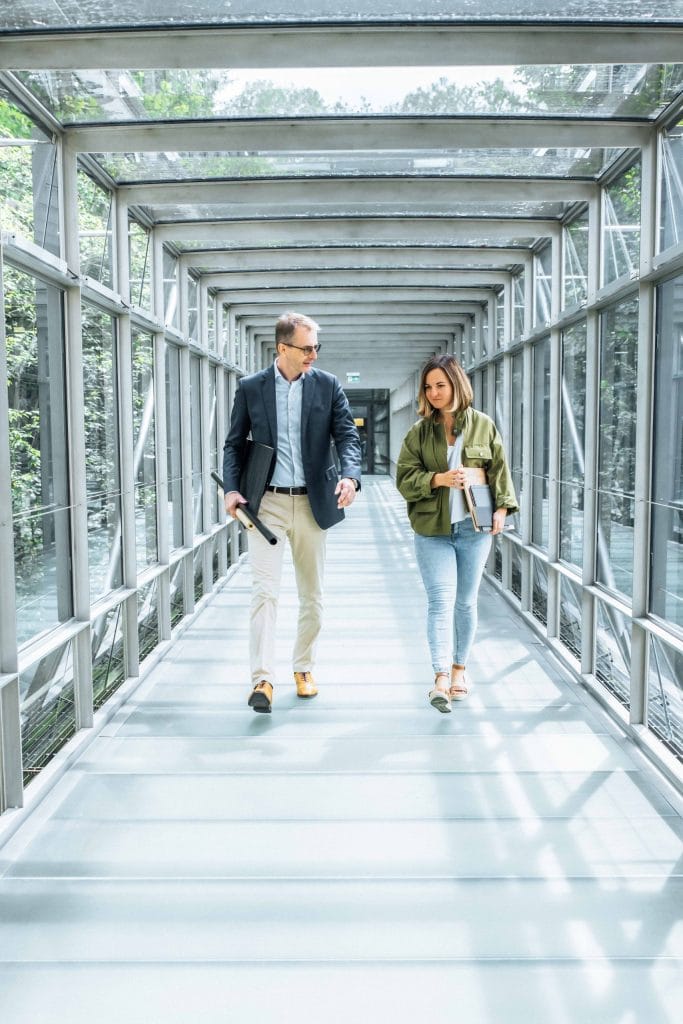 zwei Personen auf dem Weg durch Schattdecor Zentrale, Holzdekor, Dekor mit Holzoptik, Schattdecor, Unternehmensfotografie, Behind The Scenes Fotografie, WINGMEN Media